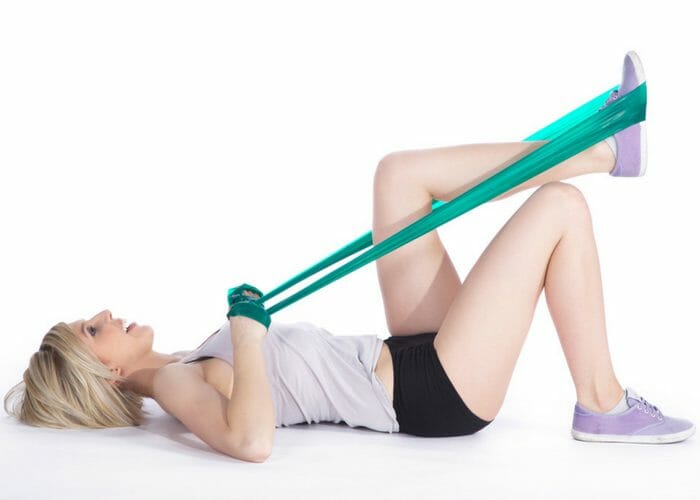 woman lying on the floor doing resistance band training with one foot