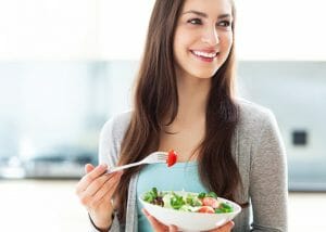 Young woman holding and eating a bowl of salad in the kitchen