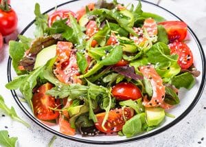 A bowl of salad with smoked salmon, mixed green leaves, tomatoes, and avocados
