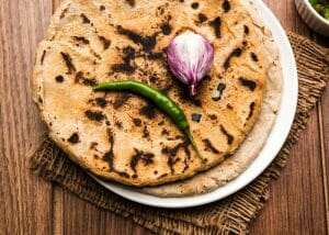 a stack of sorghum flour naan bread on a plate with a green chili and onion on top of it
