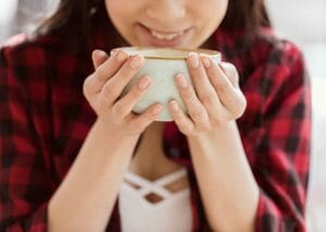 woman smiling and holding a mug of coffee with both hands