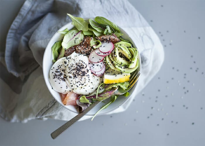 Spinach and poached egg Keto breakfast bowl topped with sesame seeds and radish