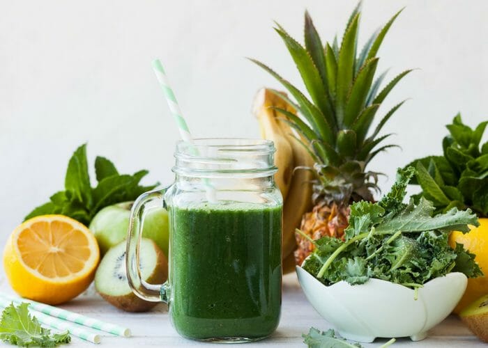 green spirulina smoothie with lemons, pineapple and leafy greens around it