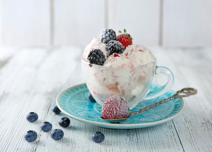 vegan gluten free vanilla ice cream in a clear teacup, on a blue dish, with berry toppings