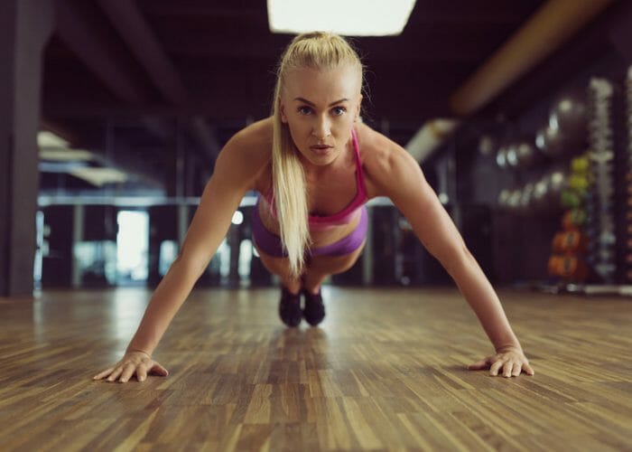 blonde woman doing planks in a gym on a wood floor