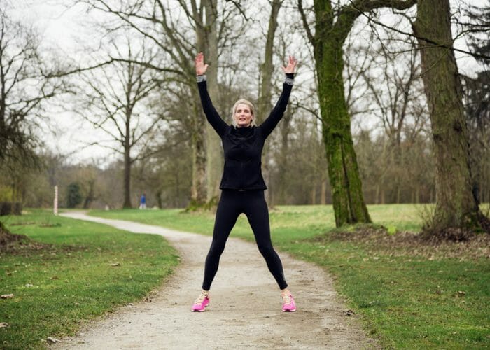 woman in a black workout suit doing jumping jacks outdoors in a park