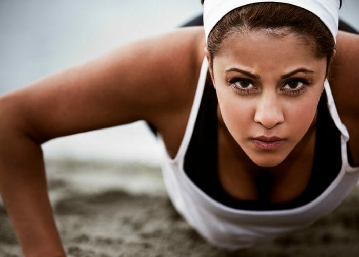 close up of a woman in workout clothes doing push ups on the sand