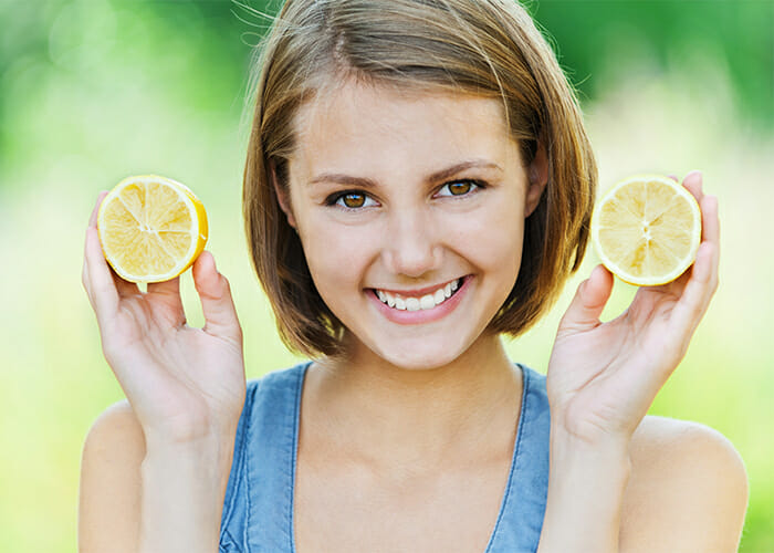 Smiling woman holding up two halves of a lemon