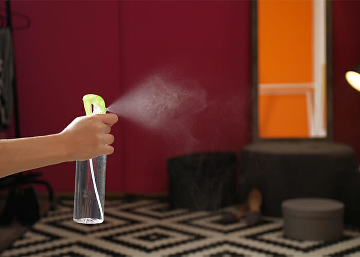 Woman spraying a bergamot essential oil room freshening spray in her home living roo