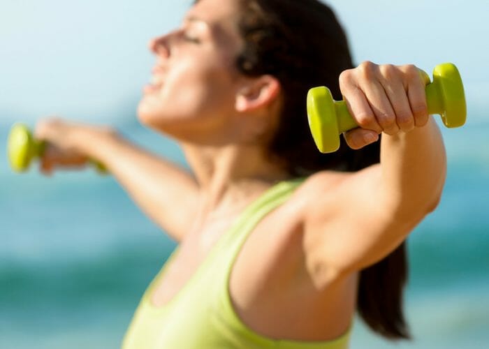 woman in green top holding small dumbbells with raised arms