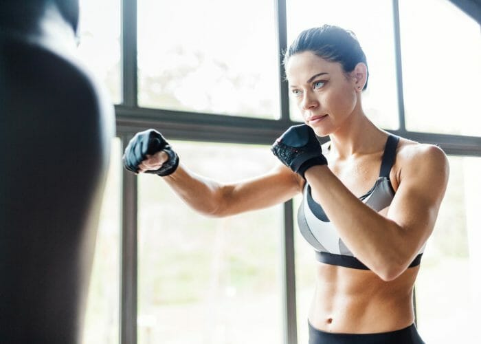 Fit woman with abs practicing kickboxing on a punching bag in a bright gym