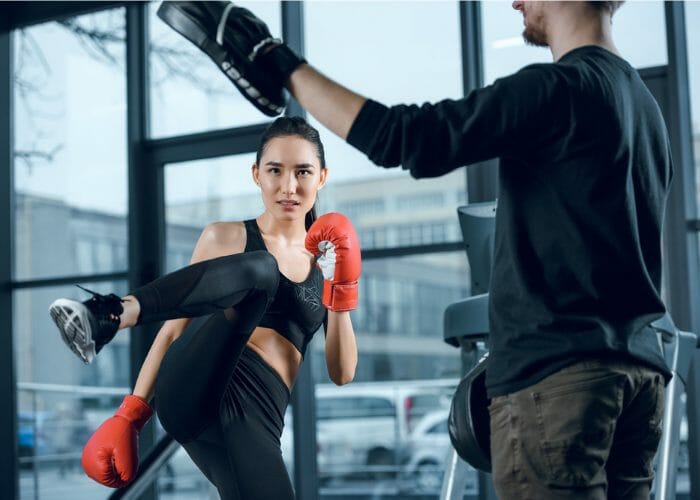 Asian woman in a gym with her kickboxing instructor attempting a high side kick