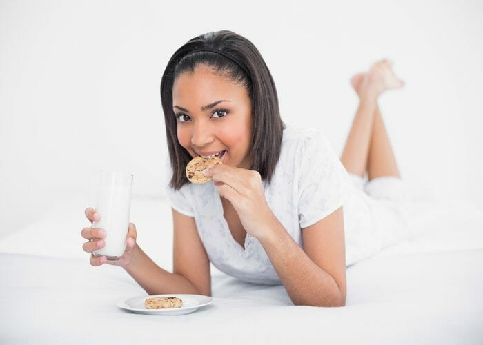 Woman eating cookies and milk in bed as a late night snack