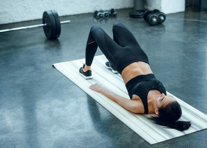 woman lying on an exercise mat with her pelvis raised doing bridges for leg exercise