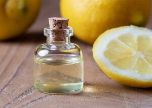 A small bottle of hand-poured lemon essential oil next to freshly cut lemons
