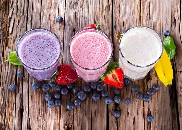 Three glasses of freshly-made fruity keto protein shake: blueberry, strawberry, and banana.