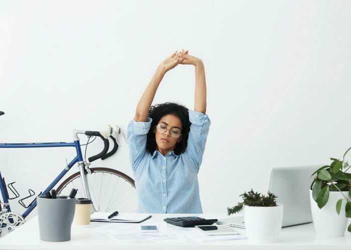 woman doing seated desk exercises stretching behind a large white office desk 