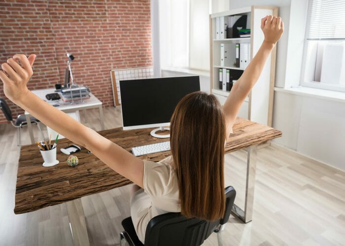 woman doing seated office exercises stretching behind a wooden desk