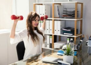 woman seated at a desk doing office exercises for arms with dumbbells