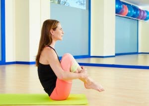 a woman sat on a pilates mat with her knees to her chest performing a pilates ball roll