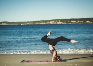 a woman on a beach performing a yoga pose on her head