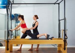 a pregnant woman doing a pilates workout with her instructor