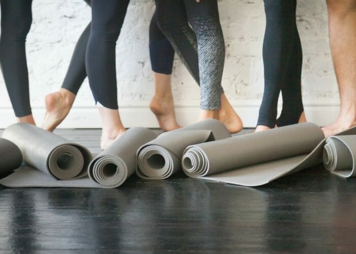 a group of women's feet standing behind rolls of grey yoga mats