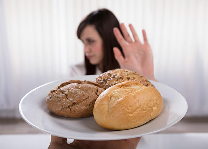 A woman on the AIP diet holding up her hand to reject a plate of three different types of bread