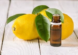 An open bottle of lemon essential oil next to two whole lemons with leaves