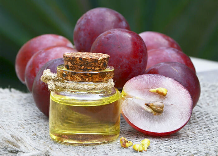 Homemade grapeseed oil in a small jar surrounded by purple grapes
