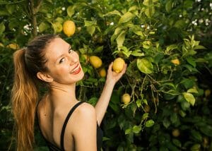 Woman smiling as she looks back while picking a lemon off of a lemon tree