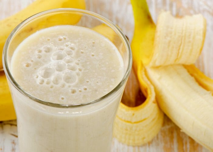 a glass of banana homemade energy drink with fresh bananas in the background