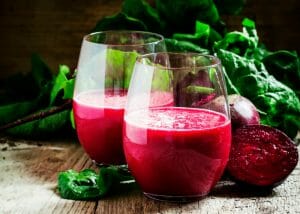 two glasses of red beet juice and the cross section of a fresh beet beside them