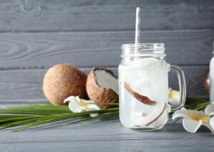 coconut water in a clear mason jar with fresh coconut pieces in it and a grey straw