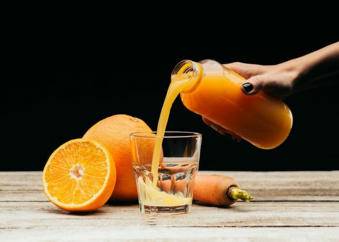 woman pouring freshly made orange homemade energy drink from a glass bottle into a glass