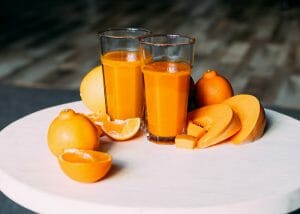 two glasses of orange juice with fresh oranges and pumpkin slices around them