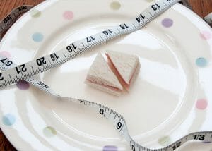 A tiny sandwich on a plate wrapped in a measuring tape to symbolize a diet with too little food