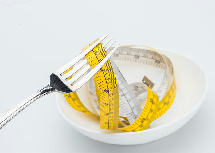 Fork picking up a measuring tape to symbolize dieting struggles
