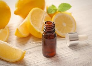 An open bottle of lemon essential oil surrounded by cut and hole lemons