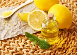 A homemade bottle of lemon essential oil presented next to lemon essential oil bath salt and fresh lemons