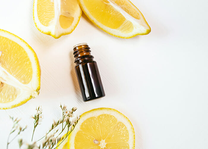 A top-down view of a bottle of lemon essential oil surrounded by cut lemons