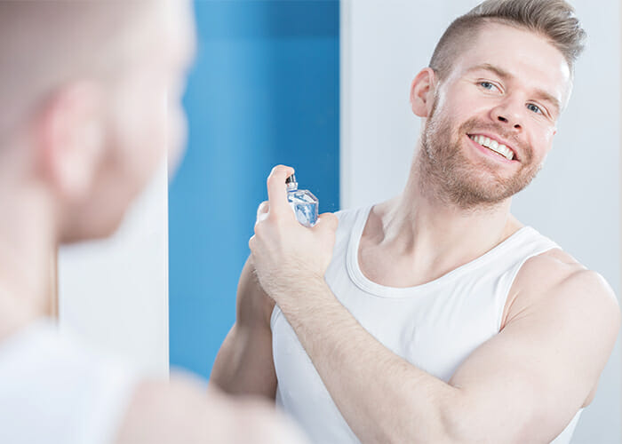 Man spraying homemade essential oil cologne on his neck while looking in the mirror