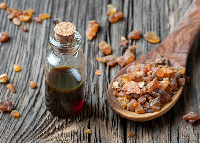 Myrrh essential oil bottle next to a wooden spoon filled with myrrh