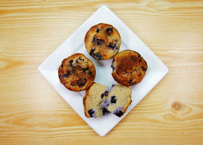 Top-down view of four homemade Paleo blueberry muffins on a white plate
