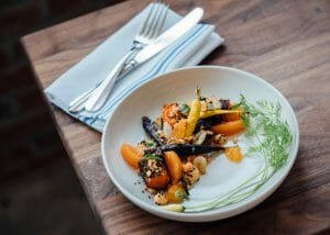 A beautifully plated dish of roasted vegetables at a fancy restaurant with cutlery beside it on a wooden table