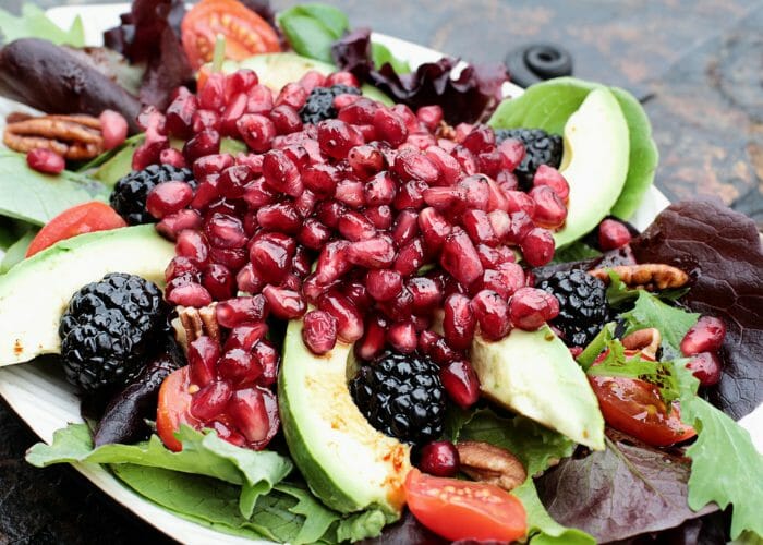 Fresh plant-based diet salad with mixed greens, walnuts, blackberries, tomatoes, topped with pomegranate.