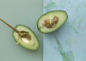 Two halves of an avocado, one set against a pastel olive green background and the other on a marble green background.