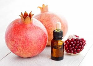 Bottle of pomegranate essential oil for wrinkle-free skin next to two fresh pomegranates
