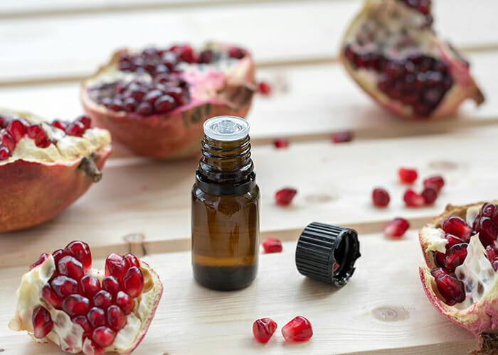 A bottle of pomegranate oil for stretch marks surrounded by freshly opened pomegranates 