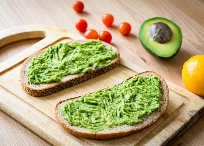 two slices of toast on a wooden board with mashed avocado spread on top of them